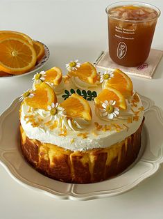 a cake with orange slices and flowers on it sitting on a plate next to a drink