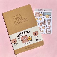 a brown notebook with stickers on it next to a pink background and coffee bear