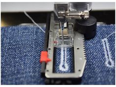 the sewing machine is working on some blue jeans with red stitchs and an orange needle