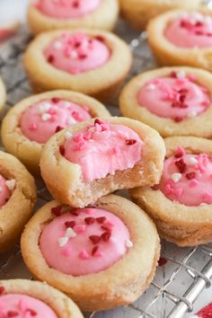 cookies with pink frosting and sprinkles are on a cooling rack, ready to be eaten