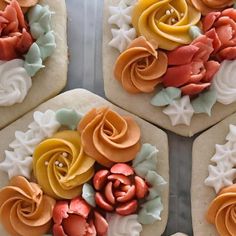 four cookies decorated with colorful icing and flowers on top of each cookie, sitting on a white plate