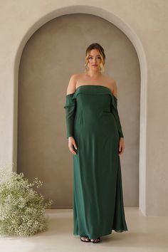 a woman in a long green dress standing next to a white plant and an archway