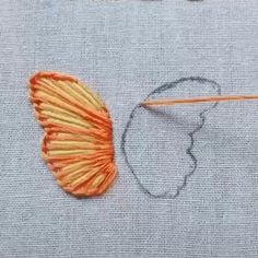 an orange piece of yarn next to a pair of scissors on a gray surface with stitches and thread