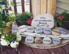 some rocks with names on them sitting in front of a wooden fence and potted plants