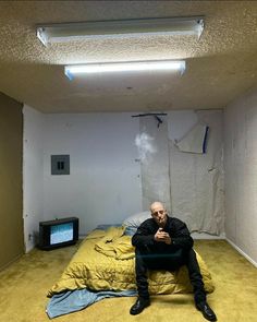 a man sitting on top of a bed in a room with yellow carpet and walls