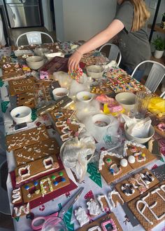 a woman is decorating gingerbreads at a table with other items on it