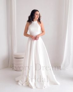 a woman in a white wedding dress standing by a window with her hands on her hips