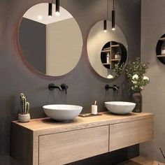 two round mirrors are above the sinks in this modern bathroom with wood flooring and gray walls