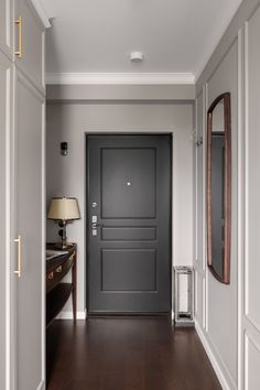 an empty hallway with a black door and wooden flooring in front of a mirror