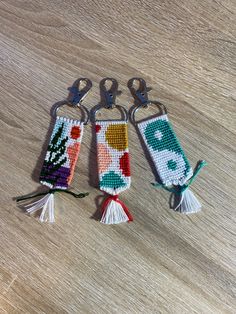 three cross stitch key fobs with tassels on them sitting on a table