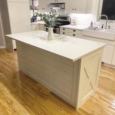 a white kitchen with wooden floors and an island in the middle of the room that has a plant on it