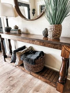 a wooden table topped with a basket next to a mirror and plant on top of it