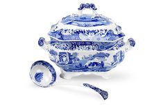 a blue and white tureen with two spoons next to it on a white background