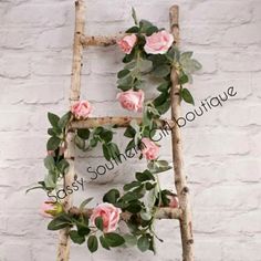 an old ladder is decorated with pink roses and greenery on the outside, against a white brick wall