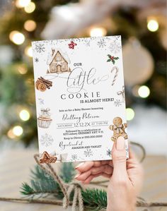 a person holding up a cookie themed birthday party card in front of a christmas tree