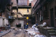 an alleyway with garbage and trash bags on the ground in front of brick buildings