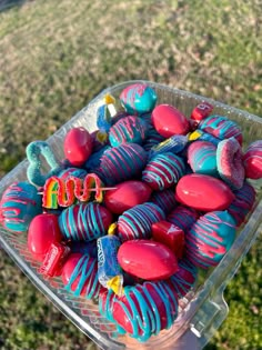 a plastic container filled with candy covered in blue and red icing on top of grass