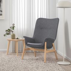 a grey chair sitting in front of a white lamp next to a table with a plant on it