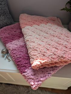 two crocheted blankets sitting on top of a white table next to a potted plant