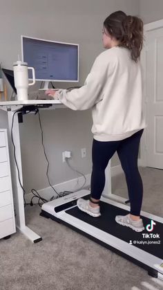 a woman standing on a treadmill using her computer