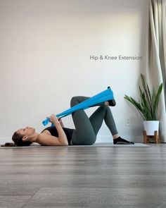 a woman is laying on the floor with a yoga mat in front of her and holding a blue exercise tube