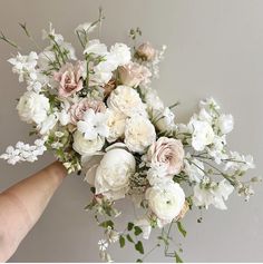 a hand holding a bouquet of white and pink flowers with greenery on the side