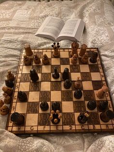 a chess board and game pieces on a bed with an open book in the background