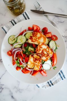 a white plate topped with vegetables and tofu on top of a table next to a fork