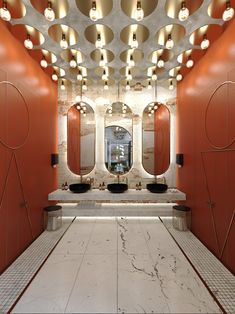 a bathroom with two sinks and mirrors on the wall, along with lights hanging from the ceiling