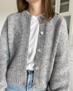 a woman is wearing a gray cardigan sweater and denim skirt with her hands in her pockets