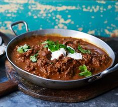 a bowl of chili with sour cream and cilantro on top, next to a bottle of wine