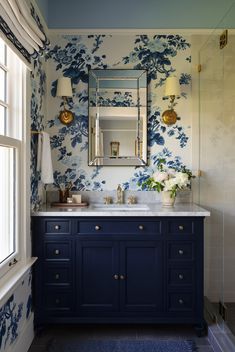 a bathroom with blue and white wallpaper, gold fixtures and a mirror above the sink