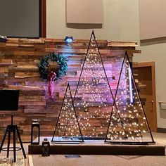 a christmas tree made out of wood with lights on the top and behind it is a projector screen