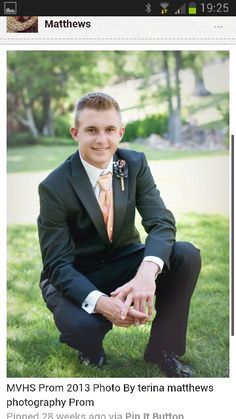 a young man in a suit and tie sitting on the grass with his hands together