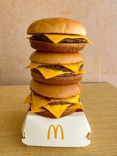 a stack of cheeseburgers sitting on top of a mcdonald's box in front of a wooden wall