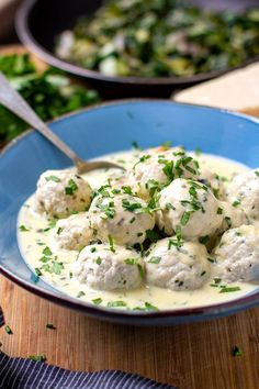 a blue bowl filled with meatballs covered in sauce and garnished with parsley