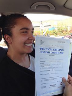 a woman holding up a driving test certificate in the back seat of a car,