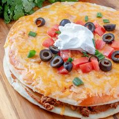 two tortillas topped with cheese, olives and sour cream on a wooden cutting board