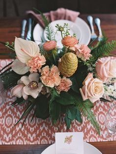 an arrangement of flowers on a table with place cards and silverware in front of it