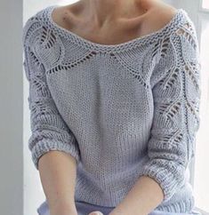 a woman sitting on a window sill wearing a sweater