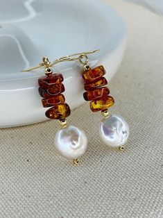 Embody elegance and natural beauty with these beautiful earrings. Handcrafted with Baltic amber gemstones and AAA coin freshwater pearls, these earrings exude sophistication. The 14K gold filled components and accessories complete the luxurious look. Elevate any outfit and feel confident in the unique benefits of our Amber Earrings. 2 1/4 inches length. I design and hand make each piece from my home studio in Port Richey Fl. I take special care in the supply of each component that will be part of the jewelry. I personally select by hand all gemstones and metals to satisfy every desire of my customers, in addition to the quality I offer in my products.  Please allow me 1-3 business days to make and package your piece(s). Your items are expected to be delivered within 7-10 business days afte Cheap Amber Jewelry Gift, Elegant Orange Pearl Drop Jewelry, Gold Pearl Earrings With Natural Stones, Elegant Baltic Amber Jewelry With Natural Stones, Elegant Orange Earrings With Natural Stones, Brown Pearl Drop Earrings As Gift, Brown Pearl Drop Earrings For Gift, Elegant Baltic Amber Dangle Jewelry, Faberge Jewelry