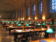 an empty library with many tables and chairs in front of large windows filled with green lamps