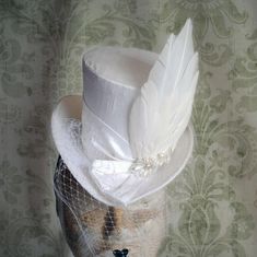 This elegant medium sized mini top hat is covered with luxurious ivory soie sauvage silk. The focal point of the decoration is a beautiful handmade dove/angel wing, placed at one side. It is further embellished with same fabric band around the crown and half bows, over the face birdcage veil and crystal and pearl hand beaded element. Measurements : height 4 inches( 10 cm ) front to back 9 inches ( 22 cm ) side to side 7.5 inches ( 19 cm ) This mini top hat is fully lined with satin and attaches Top Hat With Veil, Ladies Wedding Hats, Fascinator With Veil, Dove Wing, Bridal Mini, Hat Veil, Bridal Fascinator, Mini Hat, Bride Hat