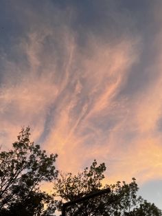 the sky is filled with pink clouds and green trees in front of it, as the sun sets