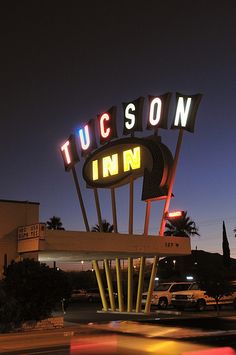 a neon sign that reads tucson inn in front of a parking lot at night