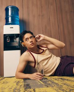 a young man laying on the floor listening to headphones next to a water dispenser