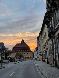 an empty street with buildings and people walking on the sidewalk in front of it at sunset