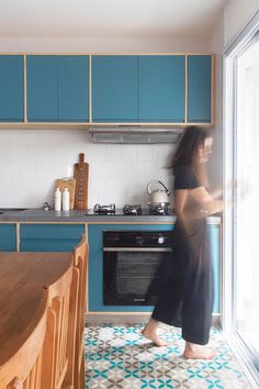 a woman standing in a kitchen next to an oven and counter top with blue cabinets