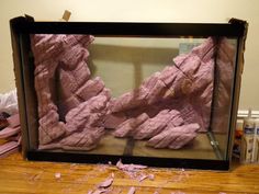 an aquarium with pink rocks in it on a wooden table next to some other items