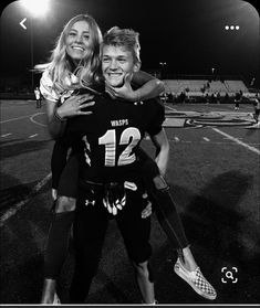 two girls hugging each other on a football field at night with lights in the background